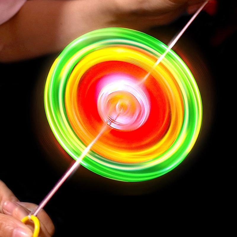 A colorful spinning yo-yo with concentric rings of green, yellow, orange, and red, photographed in motion against a black background with hands holding the string.