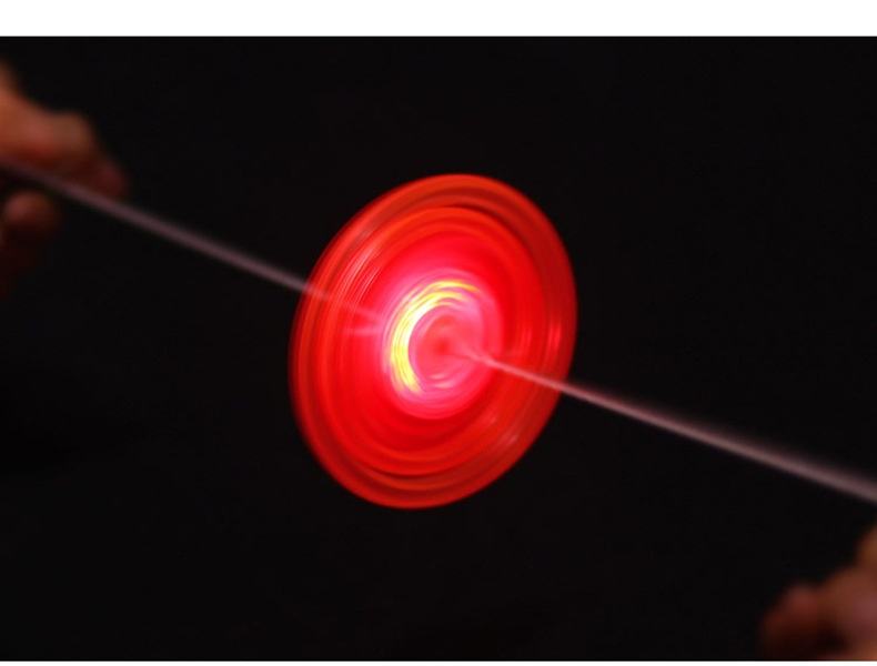 A glowing red and orange spinning disc toy, likely a light-up yo-yo or LED spinner, captured in motion against a solid black background with fingers visible on the left and right edges holding the string.