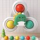A children's toy fidget spinner with a cute green dinosaur character in the center, featuring three circular spinner arms with red, yellow, and teal buttons, shown against a white tiled wall background.