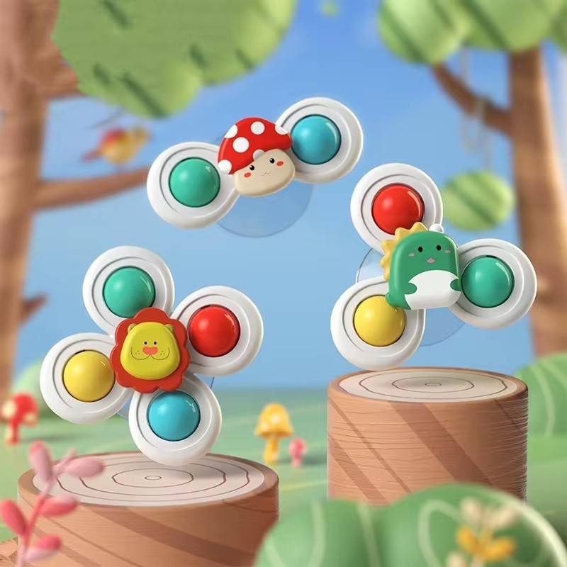 Three colorful children's toy fidget spinners with cartoon animal and mushroom faces, displayed on wooden logs against a soft outdoor forest background.