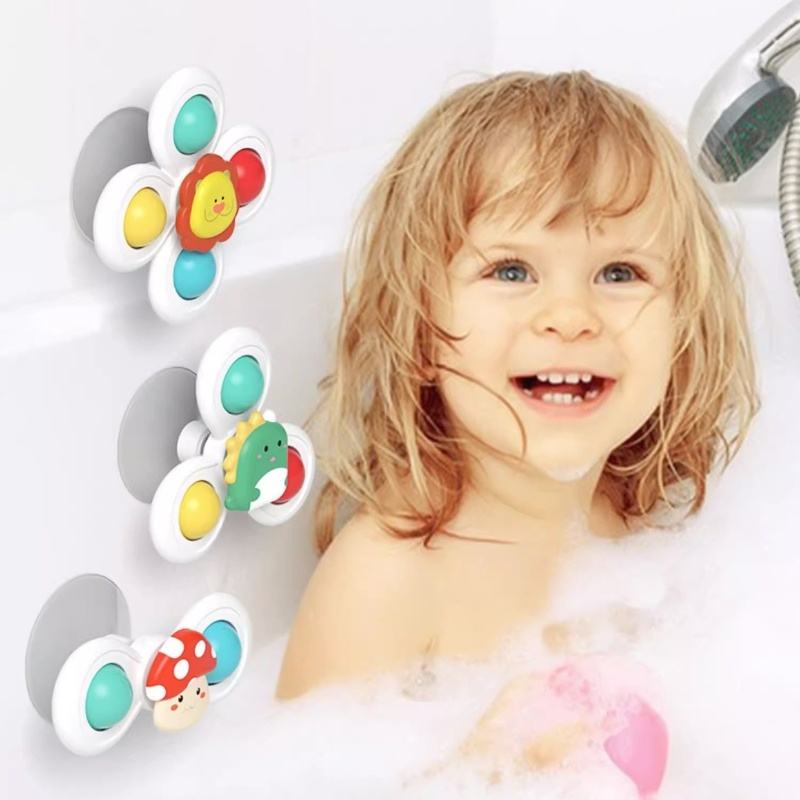 Three colorful suction cup bath toys with animal and mushroom designs are shown on a white bathtub next to a smiling young child in bubble bath water.