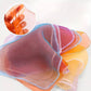 A stack of sheer mesh underwire bra cups in assorted pastel and bright colors, each with a white scalloped trim, shown on a white background. A circular inset in the top left shows a hand stretching the elastic band of one cup to demonstrate flexibility.