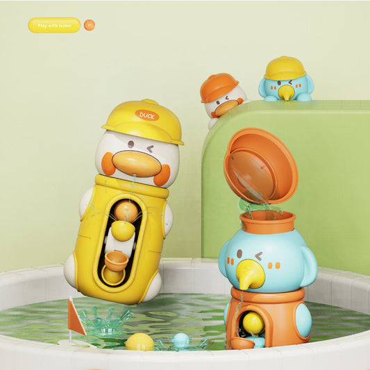 Two cartoon duck-shaped bath toys in a white tub with water. One yellow duck toy holds a ball and wears a construction helmet, while the blue and orange duck toy has its bucket tipped over with water running into the orange container.