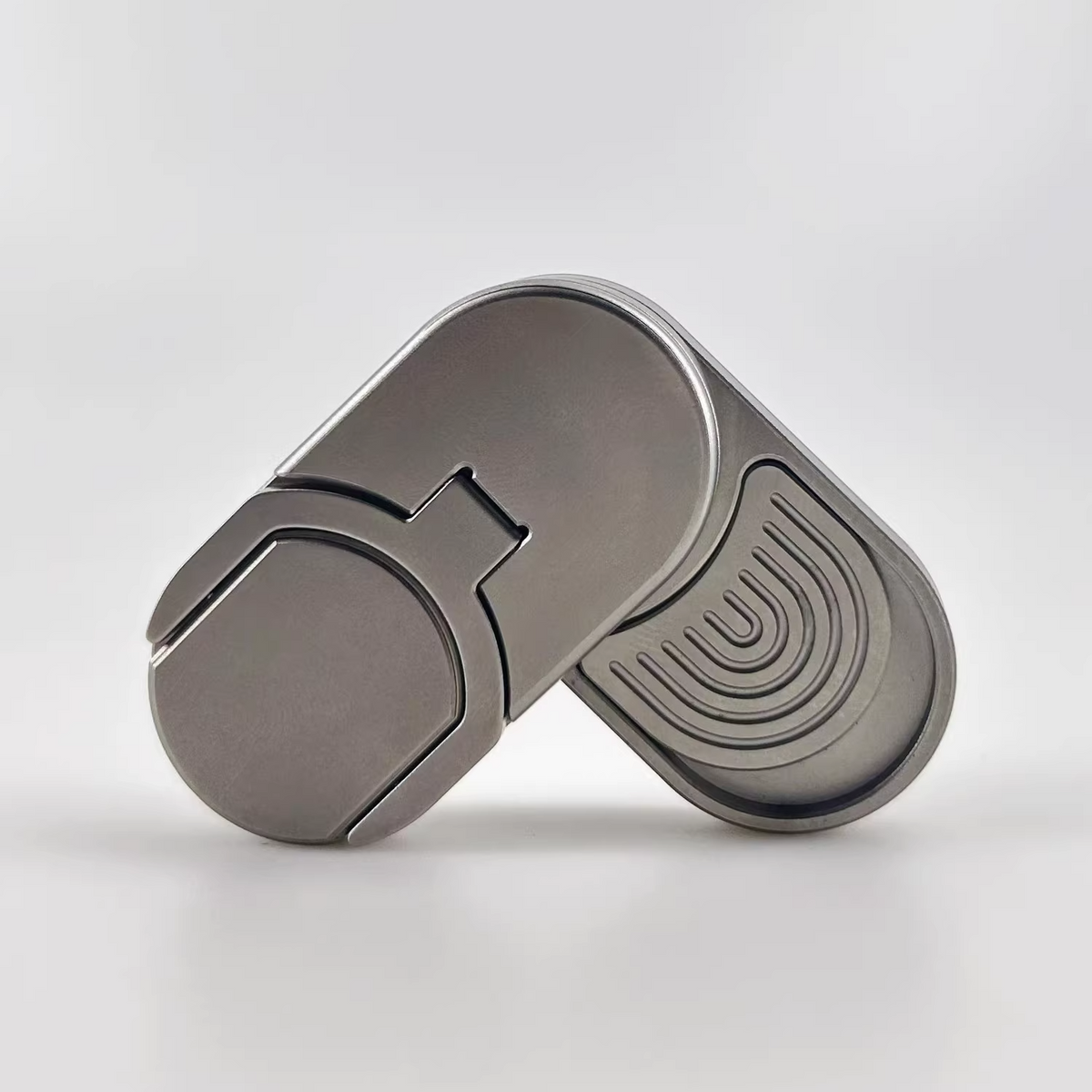 A metallic gray fidget spinner with a smooth oval body, featuring a split design with one half showing a smooth surface and the other half displaying concentric arches.