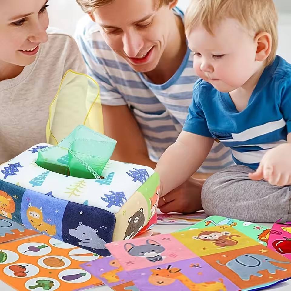 A baby toy puzzle book with colorful animal and vegetable illustrations is being played with by a baby and a smiling man, with a woman partially visible on the left.