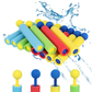A set of colorful foam pool noodles and water guns shown on a white background with a blue water splash graphic behind them. The main product consists of multiple cylindrical foam pieces in blue, green, red, and yellow, with some pieces featuring blue and yellow ball-tooth ends, and additional toy water guns shown below.