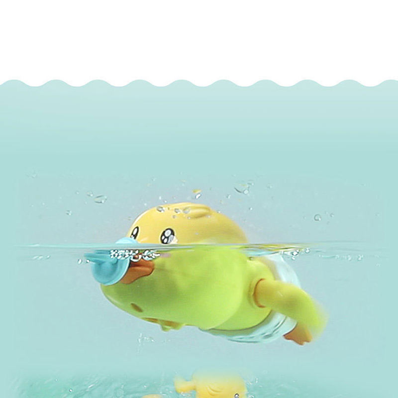 A yellow duck-shaped baby bath toy floating underwater, holding a blue pacifier in its beak. The toy has a white diaper and is shown in a light aqua water setting with a white background above the waterline.
